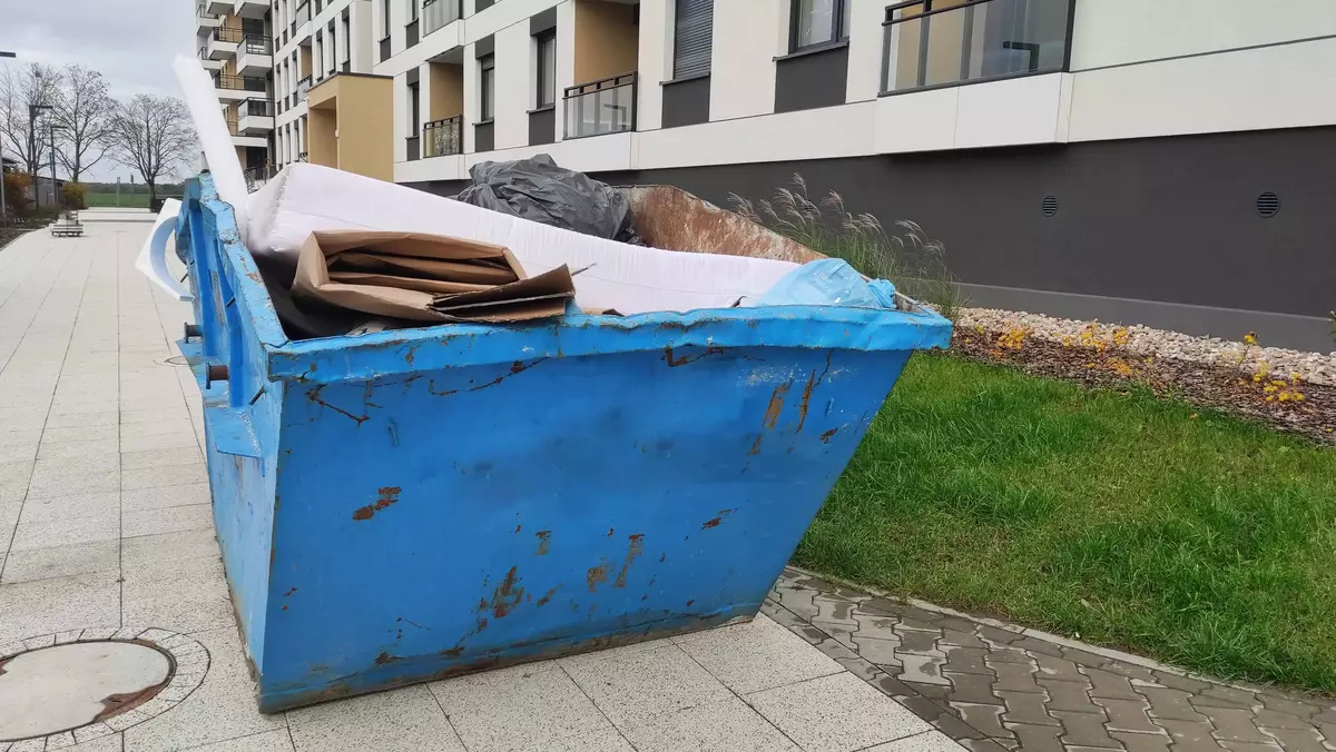 Blue dumpster with waste materials outside a building